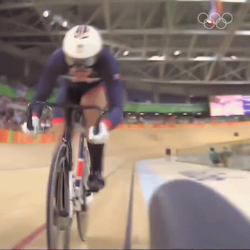 A Person Riding A Bike In A Stadium With The Olympic Rings In The Background GIF