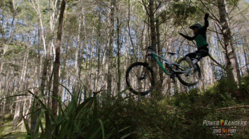A Person Riding A Bike In The Woods With A Power Rangers Logo In The Background GIF
