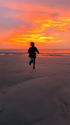 A Person Running On A Beach With A Sunset In The Background GIF