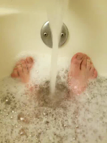 A Person 'S Feet Are Floating In A Bathtub Filled With Foam . GIF