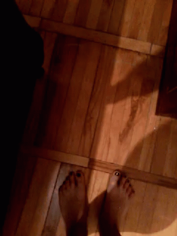 A Person 'S Feet Are Standing On A Wooden Floor In A Dark Room GIF