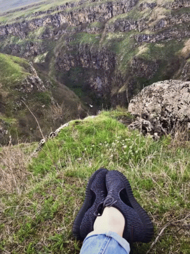 A Person 'S Feet Rest On A Grassy Hillside Overlooking A Valley GIF