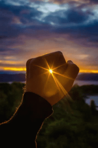 A Person 'S Fist Is Holding The Sun In Front Of A Sunset GIF
