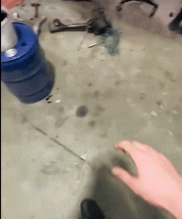 a person 's hand is reaching for a blue barrel on a dirty floor