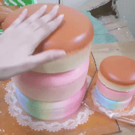 A Person 'S Hand Is Reaching Into A Stack Of Colorful Cakes On A Table GIF