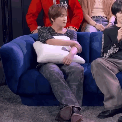 A Person Sitting On A Blue Couch With A Pillow On Their Lap GIF