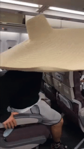 A Person Sitting On An Airplane With A Large Blanket Over Their Head GIF