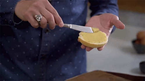 A Person Spreading Butter On A Slice Of Bread With A Knife GIF