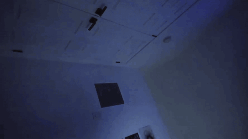 A Person Standing In A Dark Room With A Blue Light On The Wall GIF