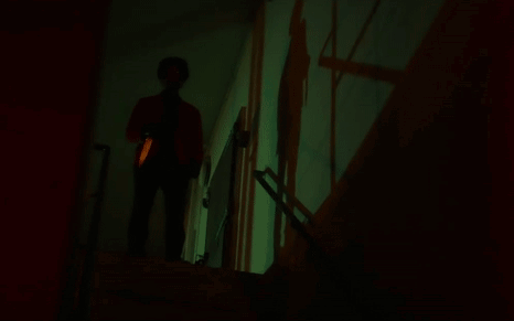 A Person Standing In A Dark Room With A Green Light Projected On The Wall GIF