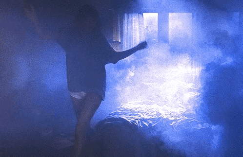 A Person Standing In A Dark Room With Blue Smoke GIF