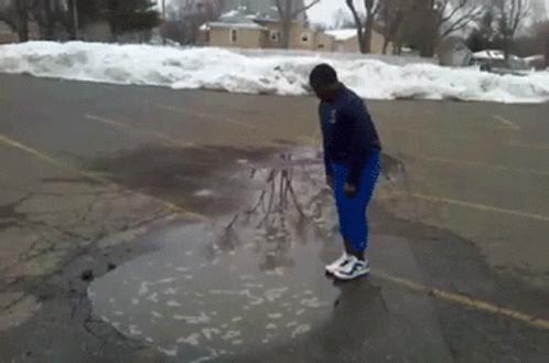A Person Standing In A Puddle In A Parking Lot With Snow On The Ground GIF
