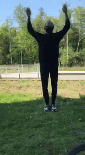 A Person Standing In The Grass With Their Arms Up In The Air GIF