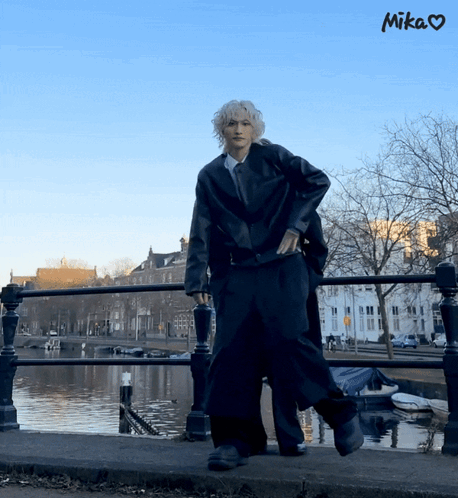 A Person Standing On A Bridge Next To A Body Of Water With The Word Mika Above Them GIF