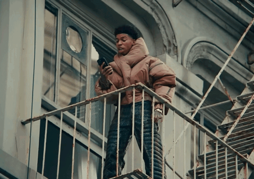 A Person Standing On A Fire Escape Looking At A Cell Phone GIF
