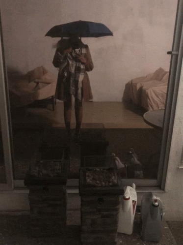 A Person Standing Under An Umbrella In A Room GIF
