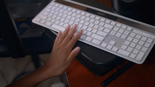 A Person Typing On A Logitech Keyboard On A Wooden Desk GIF