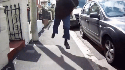 A Person Walking Down A Street With A Car Parked On The Side GIF