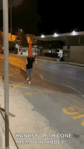 A Person Walking Down A Street With A Traffic Cone On Their Head And The Words Thanks For The Cone Removal Abbey GIF
