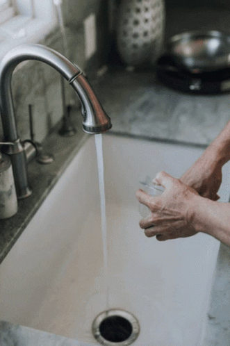 A Person Washing Their Hands In A Sink With Water Running GIF
