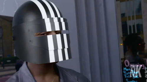 A Person Wearing A Black Helmet With White Stripes On It Stands In Front Of A Sign That Says The Nk GIF