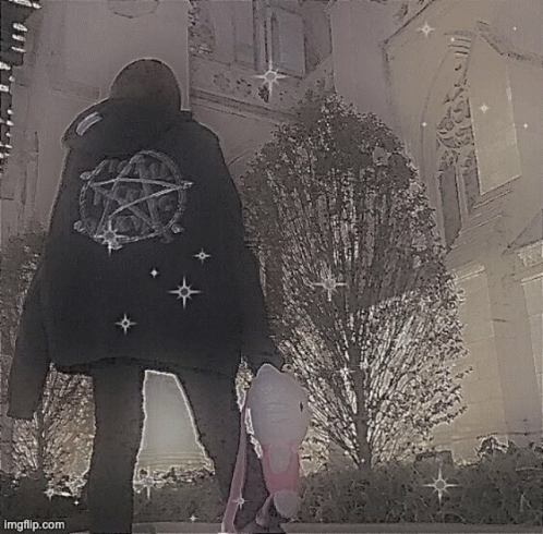 A Person Wearing A Black Jacket With A Pentagram On The Back Is Standing In Front Of A Building . GIF