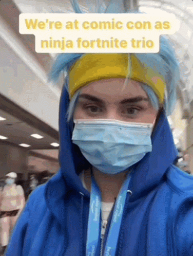 A Person Wearing A Blue Hoodie And A Mask Is Standing In A Hallway . GIF