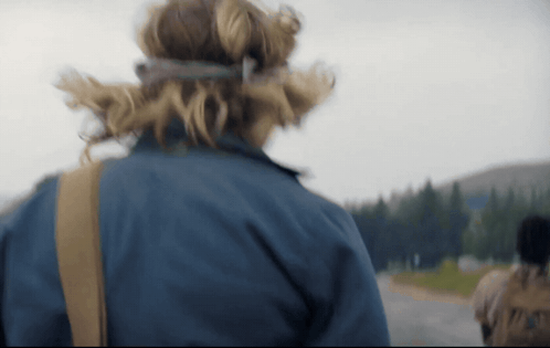 A Person Wearing A Blue Jacket Is Walking Down A Road With Trees In The Background GIF