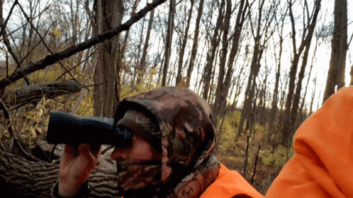 A Person Wearing A Camo Hooded Jacket Looking Through Binoculars GIF