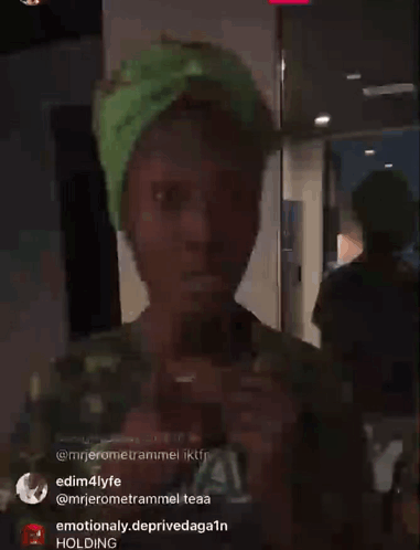 A Person Wearing A Green Hat Is Standing In A Room With A Holding Sign In The Corner GIF