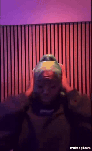 A Person Wearing A Green Hat Is Standing In Front Of A Purple And Red Wall . GIF