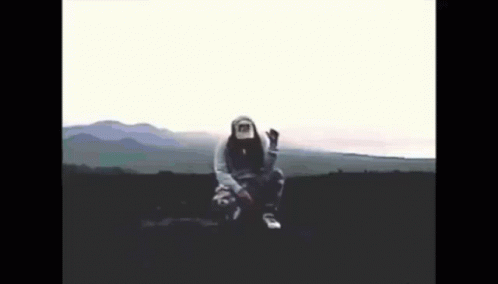 A Person Wearing A Hoodie And A Hat Is Sitting In The Middle Of A Field GIF