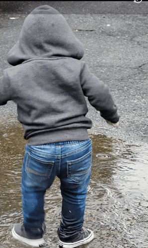 A Person Wearing A Hoodie And Jeans Standing In A Puddle Of Water GIF