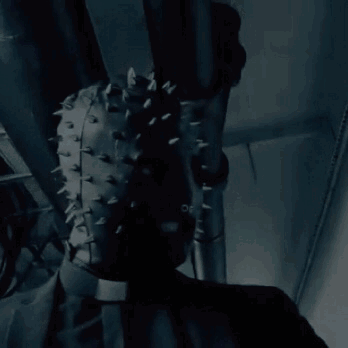 A Person Wearing A Leather Mask With Spikes On It Is Hanging From A Pipe . GIF
