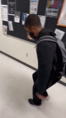 A Person Wearing A Mask And A Backpack Is Walking Down A Hallway GIF