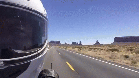A Person Wearing A Motorcycle Helmet Is Driving Down A Desert Road GIF