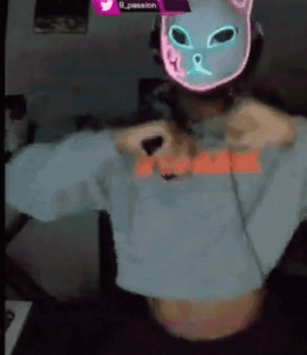 A Person Wearing A Neon Cat Mask And A Crop Top Is Taking Off Their Shirt . GIF