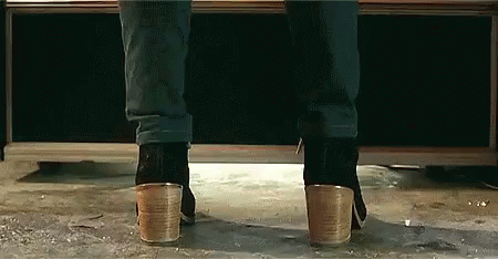 A Person Wearing A Pair Of Heeled Boots Is Standing On A Concrete Floor . GIF
