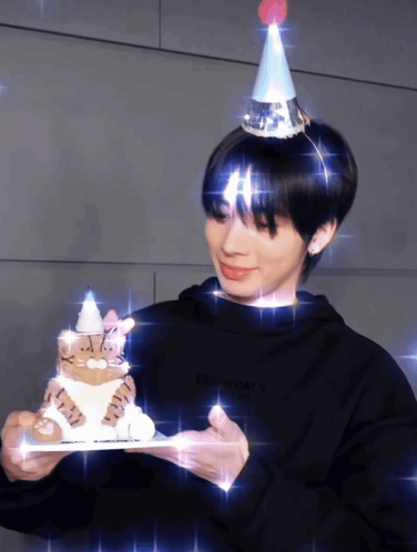 A Person Wearing A Party Hat Is Holding A Cake GIF