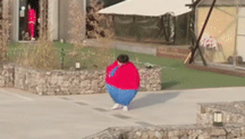 A Person Wearing A Red Sweater And Blue Pants Is Standing On A Sidewalk . GIF