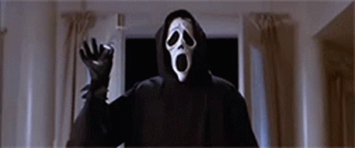 A Person Wearing A Scream Mask And A Hooded Jacket Is Standing In A Dark Room . GIF