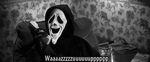 A Person Wearing A Scream Mask Is Talking On A Cell Phone While Sitting On A Couch . GIF
