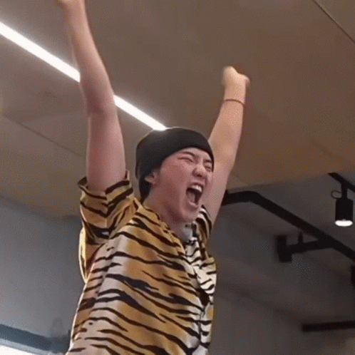 A Person Wearing A Tiger Print Shirt And A Black Beanie Is Raising Their Arms In The Air GIF