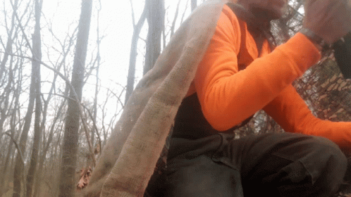 A Person Wearing An Orange Shirt And Black Pants Is Sitting In The Woods GIF