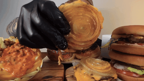A Person Wearing Black Gloves Is Holding A Piece Of Cheese On A Hamburger GIF