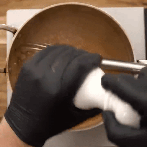 A Person Wearing Black Gloves Is Mixing Something In A Pot With A Blender . GIF