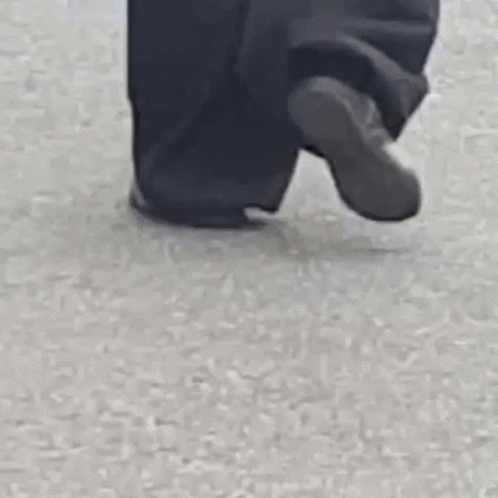 A Person Wearing Black Pants And A White Jacket Is Walking On A Street . GIF