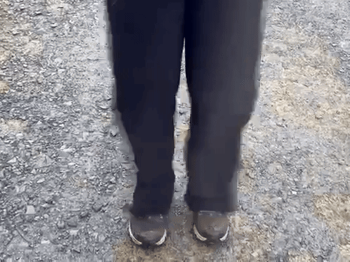 A Person Wearing Black Pants And Brown Shoes Is Standing On A Gravel Path GIF