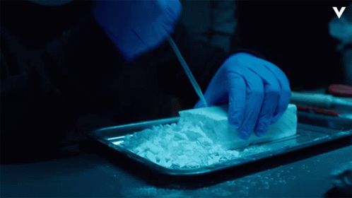 A Person Wearing Blue Gloves Is Cutting Up A Piece Of White Powder GIF
