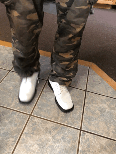 A Person Wearing Camo Pants And White Shoes Stands On A Tiled Floor GIF